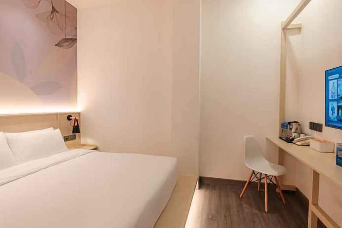 Habitación de hotel con cama, escritorio con silla, lámpara de escritorio y televisor montado en la pared.