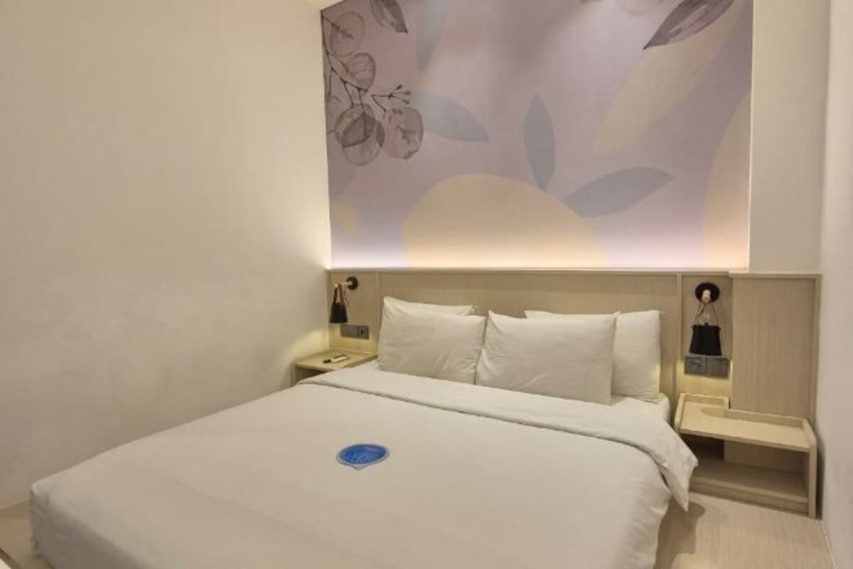 A hotel room with a large bed, a nightstand, a wall-mounted lamp, and a floral wall decoration.