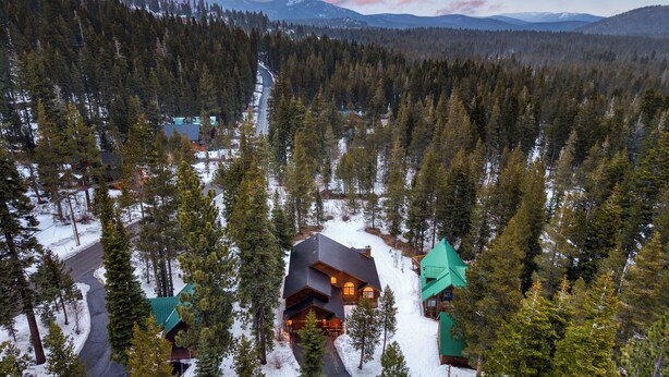 Una cabaña con un edificio central rodeado de terreno cubierto de nieve y un bosque denso.