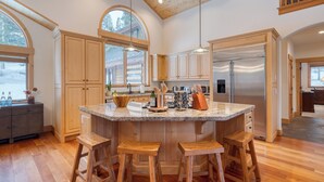 Una cocina amplia con armarios de madera, una isla grande con taburetes, electrodomésticos de acero inoxidable y ventanas grandes.