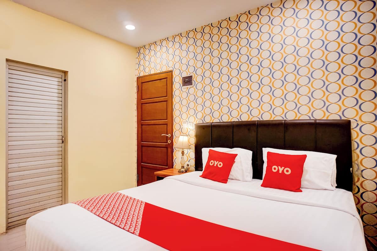 A hotel room with a bed, two red pillows with "OYO" text, a patterned wall, and a wooden door.