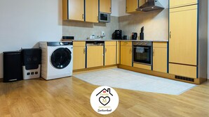 Een moderne keuken met houten kastjes, een magnetron, een wasmachine en een fornuis.
