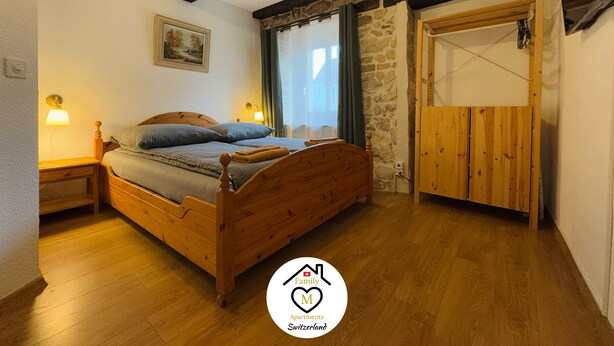Een slaapkamer met een houten bed, een stenen muur, een houten deur en een schilderij aan de wand.