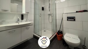 Een moderne badkamer met een douche met glazen wand, een witte wastafel en een toilet.