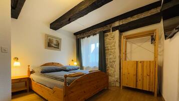 Een slaapkamer met een houten bed, een stenen muur, een houten deur en een schilderij aan de wand.