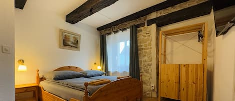 A bedroom with a wooden bed, a stone wall, a wooden door, and a painting on the wall.