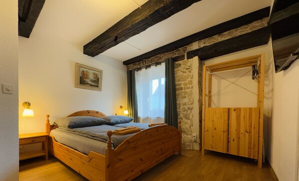 A bedroom with a wooden bed, a stone wall, a wooden door, and a painting on the wall.