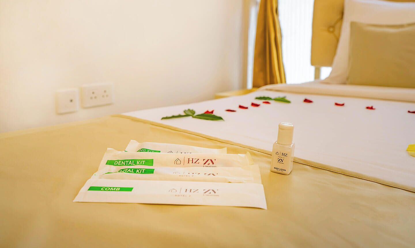 A hotel room with a neatly made bed, a bedside table with toiletries, and a wall socket.