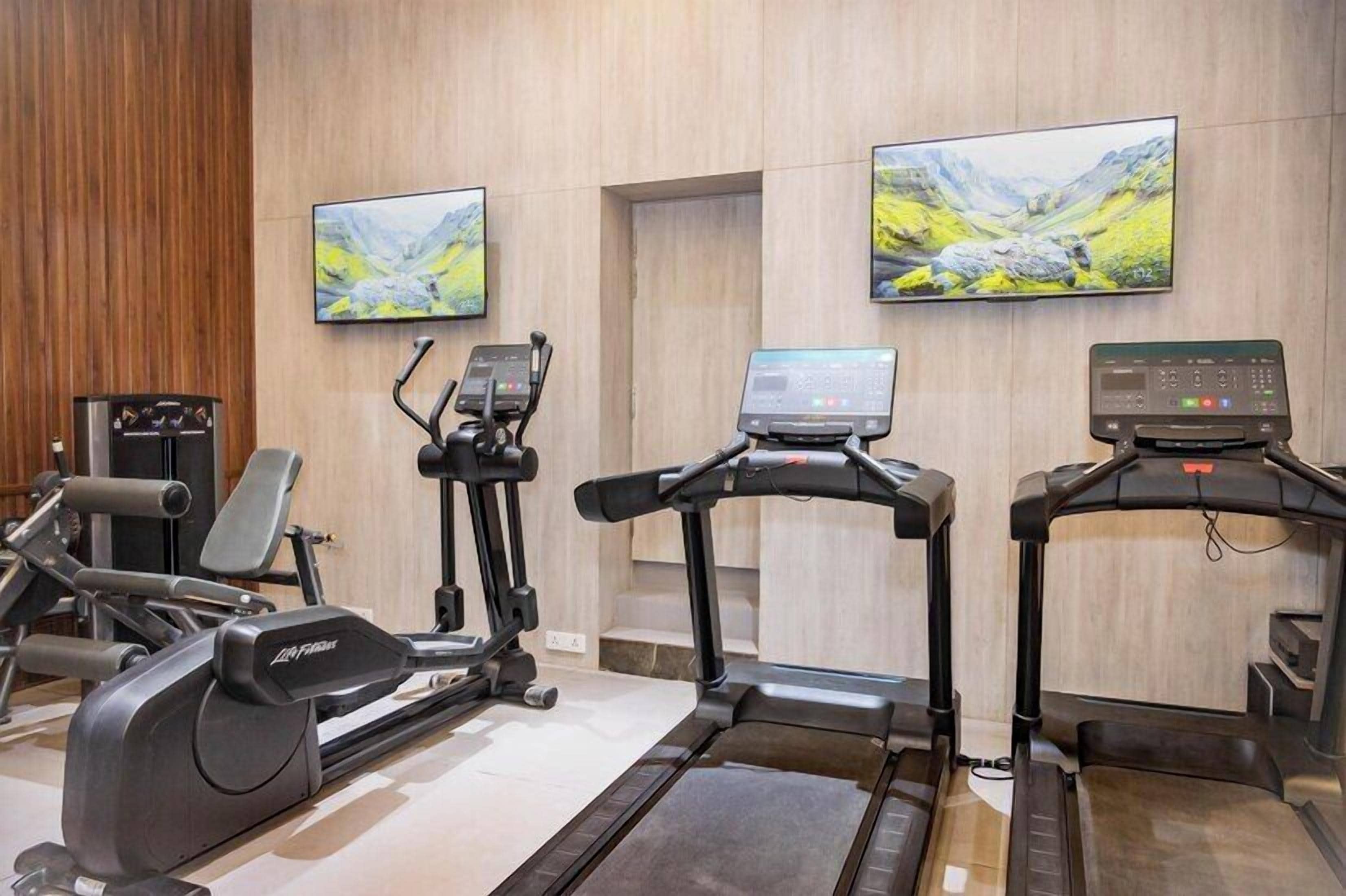 A gym with exercise equipment, a treadmill, and two wall-mounted televisions.