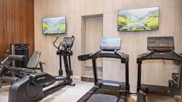 A gym with exercise equipment, a treadmill, and two wall-mounted televisions.