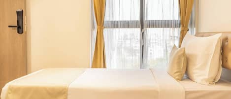 A single bed with a headboard, a wooden door, and sheer curtains.