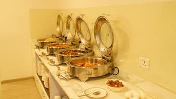 A buffet setup with multiple stainless steel bowls containing various dishes, a marble countertop, and a wall socket.