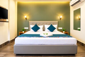 A modern hotel room with a large bed, two bedside tables, a flat-screen TV, and a wall-mounted air conditioner. - Arooba Residency Calangute (Calangute)