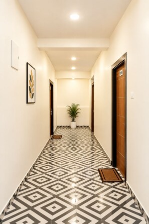 A hallway with patterned flooring, a potted plant, and doors marked with numbers. - Arooba Residency Calangute (Calangute)