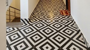 A hallway with a geometric patterned floor, a staircase on the left, and a wooden door at the end. - Arooba Residency Calangute (Calangute)