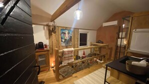 L’intérieur d’un chalet rustique, avec un escalier en bois, un mur en pierre, un tableau et un petit coin cuisine comprenant un panier et une serviette.