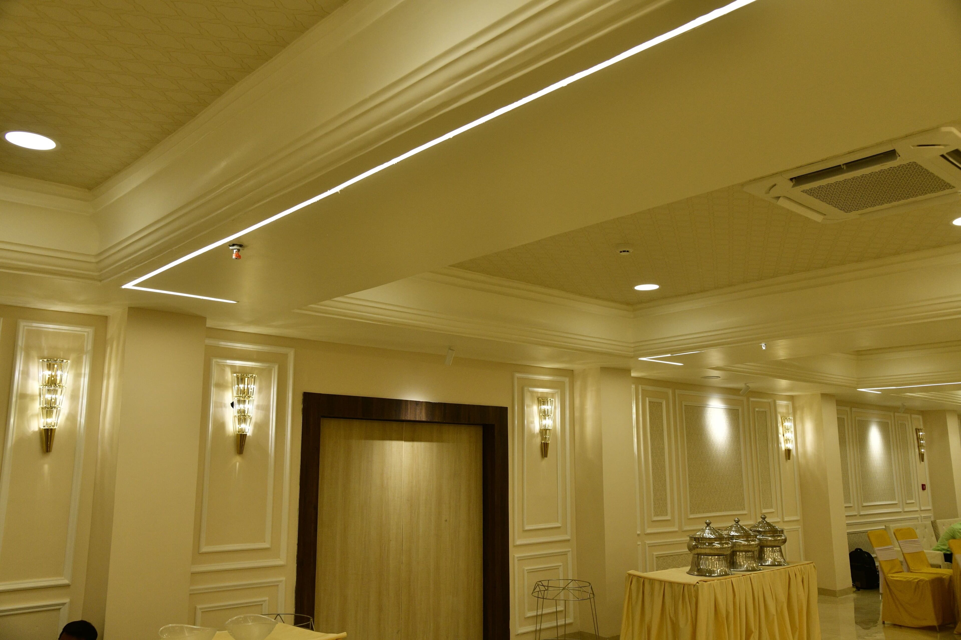 A hotel lobby with a high ceiling, recessed lighting, a reception desk, and a buffet table.