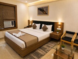A hotel room with a large bed, bedside tables, a glass coffee table, a chair, and a wall-mounted air conditioner.