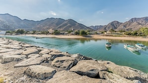 A river with boats, rocky shore, and mountains in the background. - Escape to a Modern 3BR Villa w/ a Private Pool & Mountain Views, Al Dana Island (Fujairah)