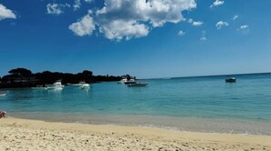 A beach with clear turquoise water, boats, and a sandy shore.
