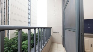 A narrow balcony with a metal railing, a white tiled wall, and a door leading to a room with a white cabinet.