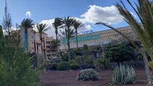 Een hotel met een reclamebord, palmbomen en cactussen op de voorgrond.