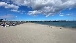 En strand med rader av blå solstolar och parasoller, en sandstrand och en klarblå himmel med moln.