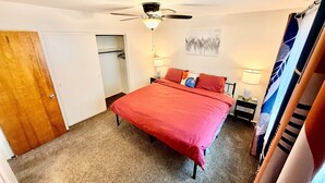 Une chambre à coucher avec un lit, un ventilateur de plafond, une table de chevet, une lampe et une porte.