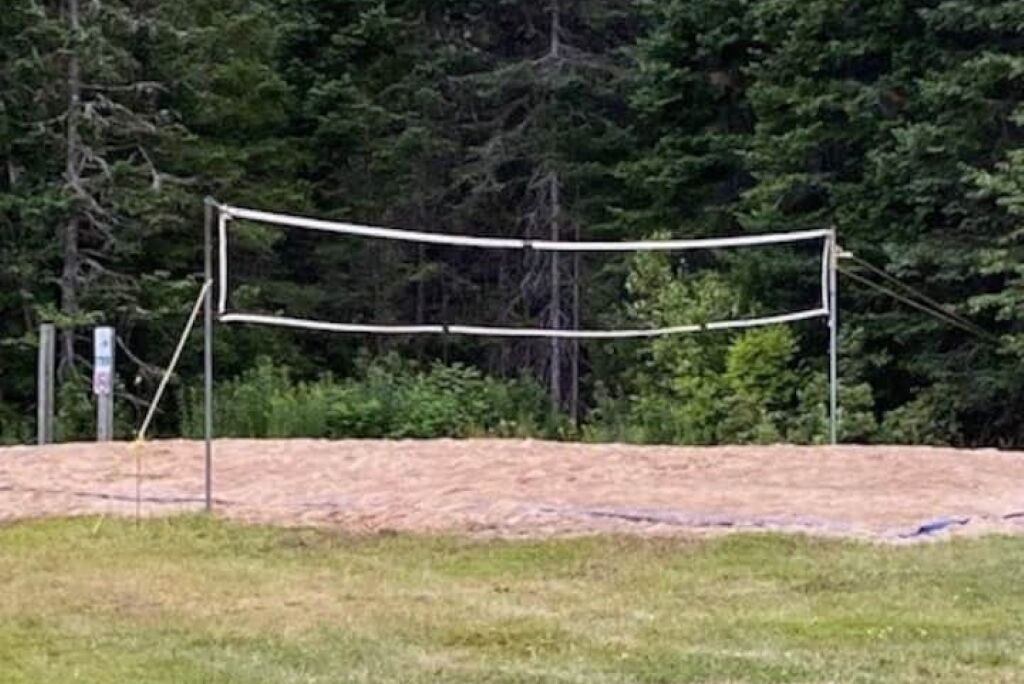 A volleyball net in a grassy area with trees in the background.
