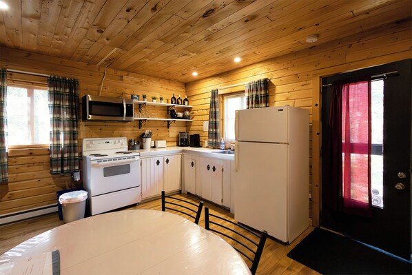 Una cocina tipo cabaña con paredes de madera, horno, microondas, refrigerador y una mesa de comedor.
