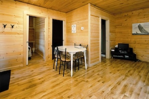 A wooden cabin interior with a dining table, chairs, a television, and a fireplace.