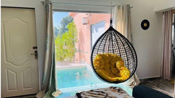 A room with a hanging chair by a window, a bed, and a door. - Jewel Stay (Manpur)
