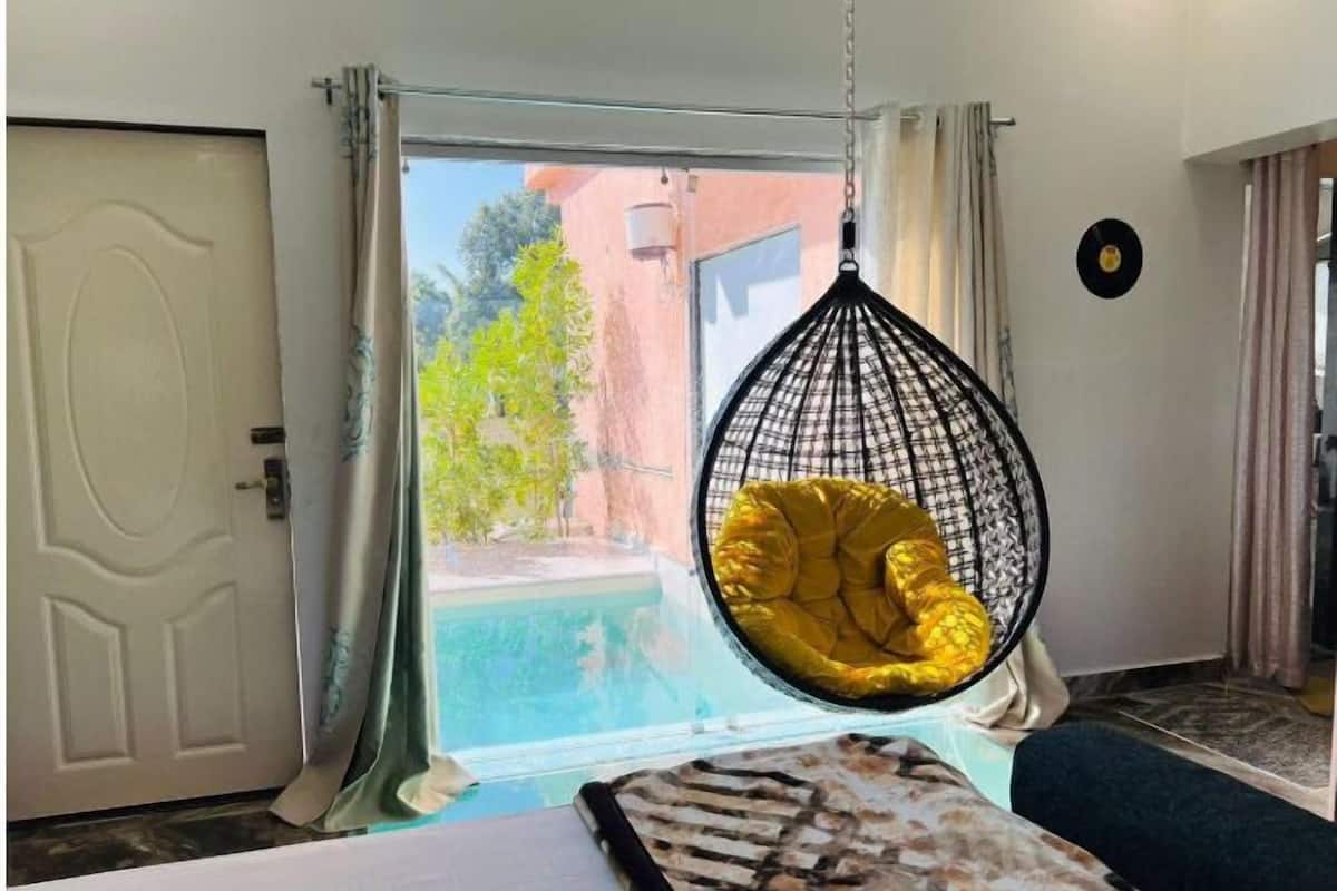Une pièce avec une chaise suspendue près d’une fenêtre, un lit et une porte.