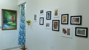 A hallway with a large painting of a tree and a river on the left, and a series of framed pictures on the right wall. - Jewel Stay (Manpur)