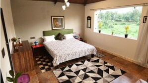 A bedroom with a bed, a nightstand, a dresser, a window with a view of greenery, and a geometric-patterned rug. - Jewel Stay (Manpur)