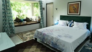 A bedroom with a bed, a window with curtains, a painting on the wall, and a door. - Jewel Stay (Manpur)
