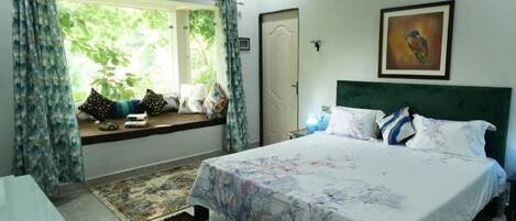 A bedroom with a bed, a window with curtains, a painting on the wall, and a door.