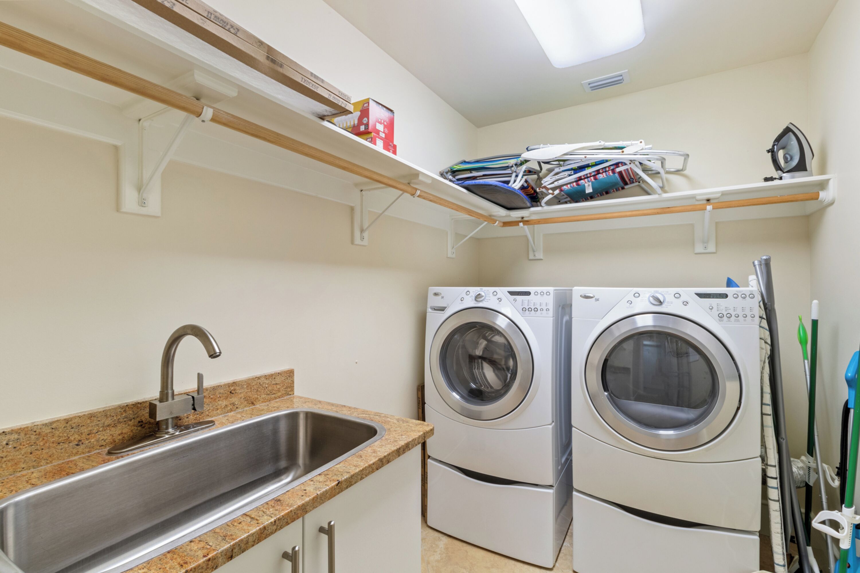 A laundry room with a washing machine, a sink, and shelves above the machine.