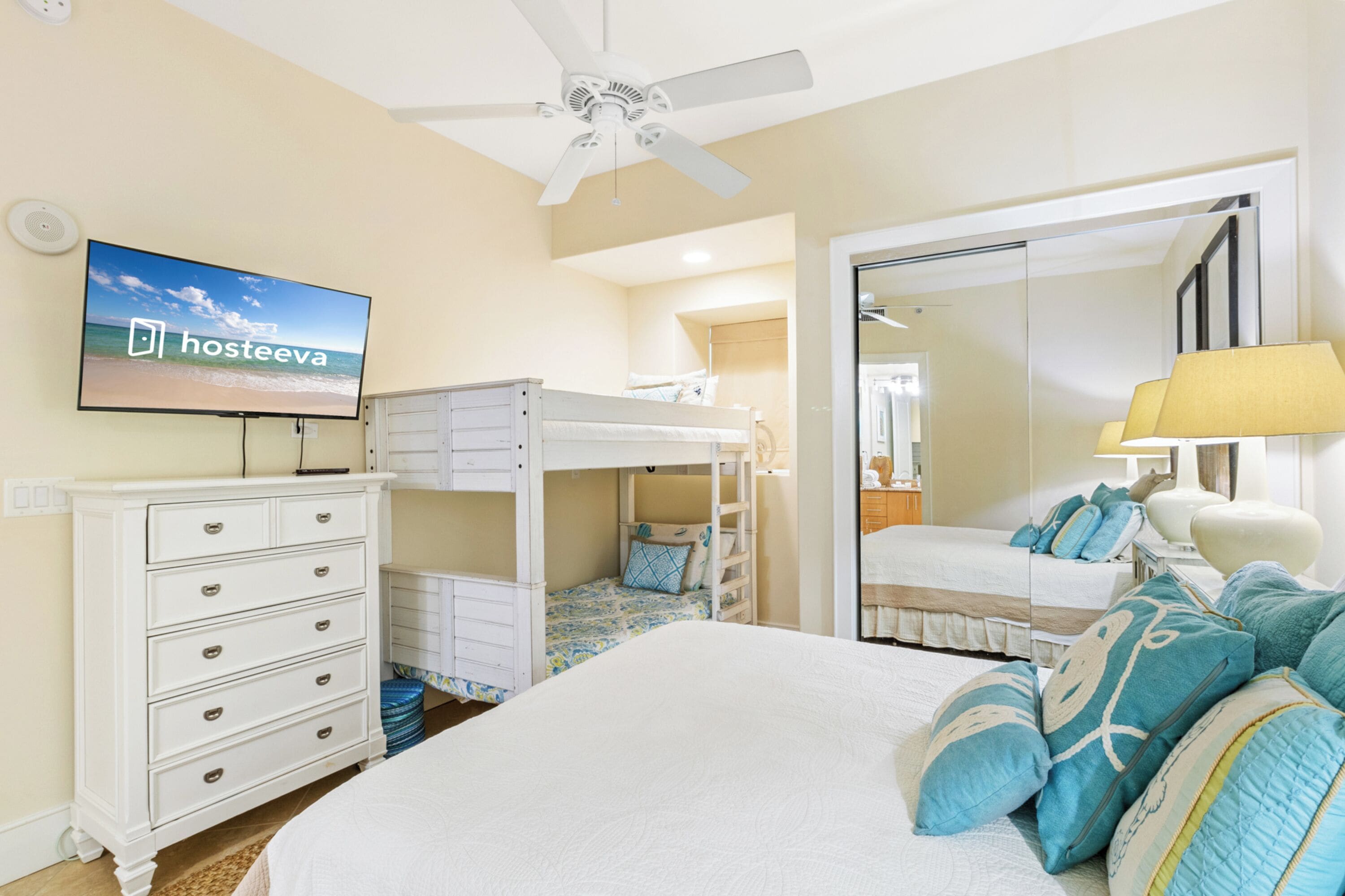 Une chambre avec des lits superposés, une télévision, une commode, un miroir et un ventilateur de plafond.