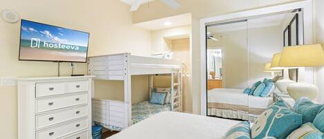 Une chambre avec des lits superposés, une télévision, une commode, un miroir et un ventilateur de plafond.
