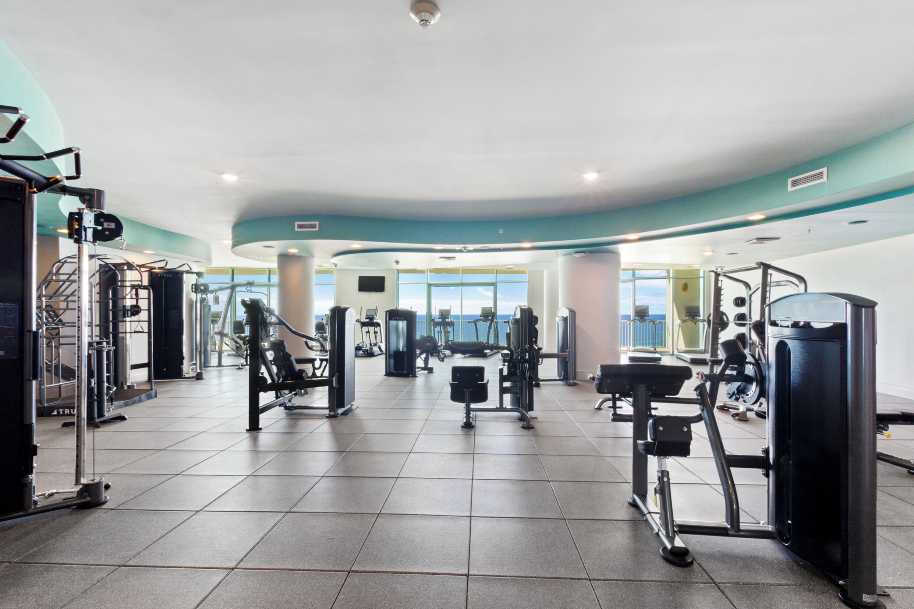 A spacious gym with various exercise equipment, large windows, and a curved ceiling.