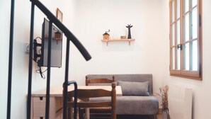 A cozy room with a wooden chair, a grey sofa, a small table, and a shelf with decorative items. - Le Colimaçon - Half-timbered house (Tours)