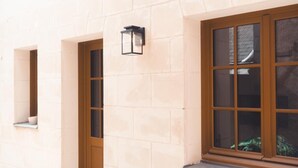 A building facade with a stone wall, a window with a wooden frame, and a wall-mounted light fixture. - Le Colimaçon - Half-timbered house (Tours)