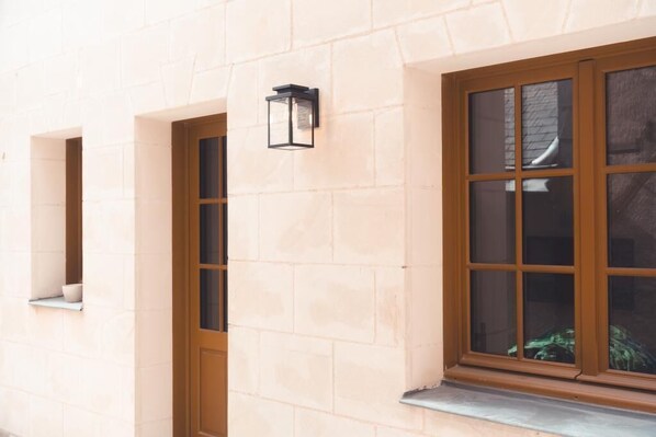 A building facade with a stone wall, a window with a wooden frame, and a wall-mounted light fixture. - Le Colimaçon - Half-Timbered House (Tours)