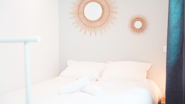 A neatly made bed with white linens, two wall-mounted sunburst mirrors, and a blue curtain on the right. - Le Colimaçon - Half-timbered house (Tours)