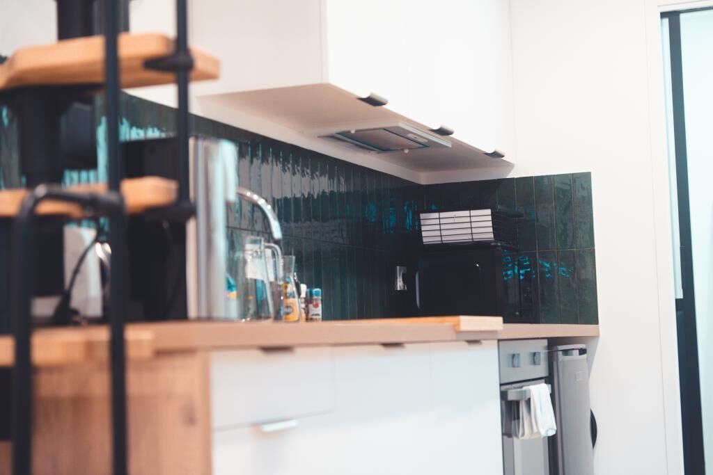 A modern kitchen with a wooden countertop, a stainless steel range hood, and a black backsplash.