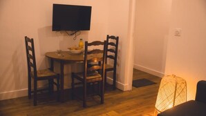 Una piccola sala da pranzo con un tavolo rotondo e quattro sedie, una televisione a schermo piatto montata a parete e una lampada da terra.