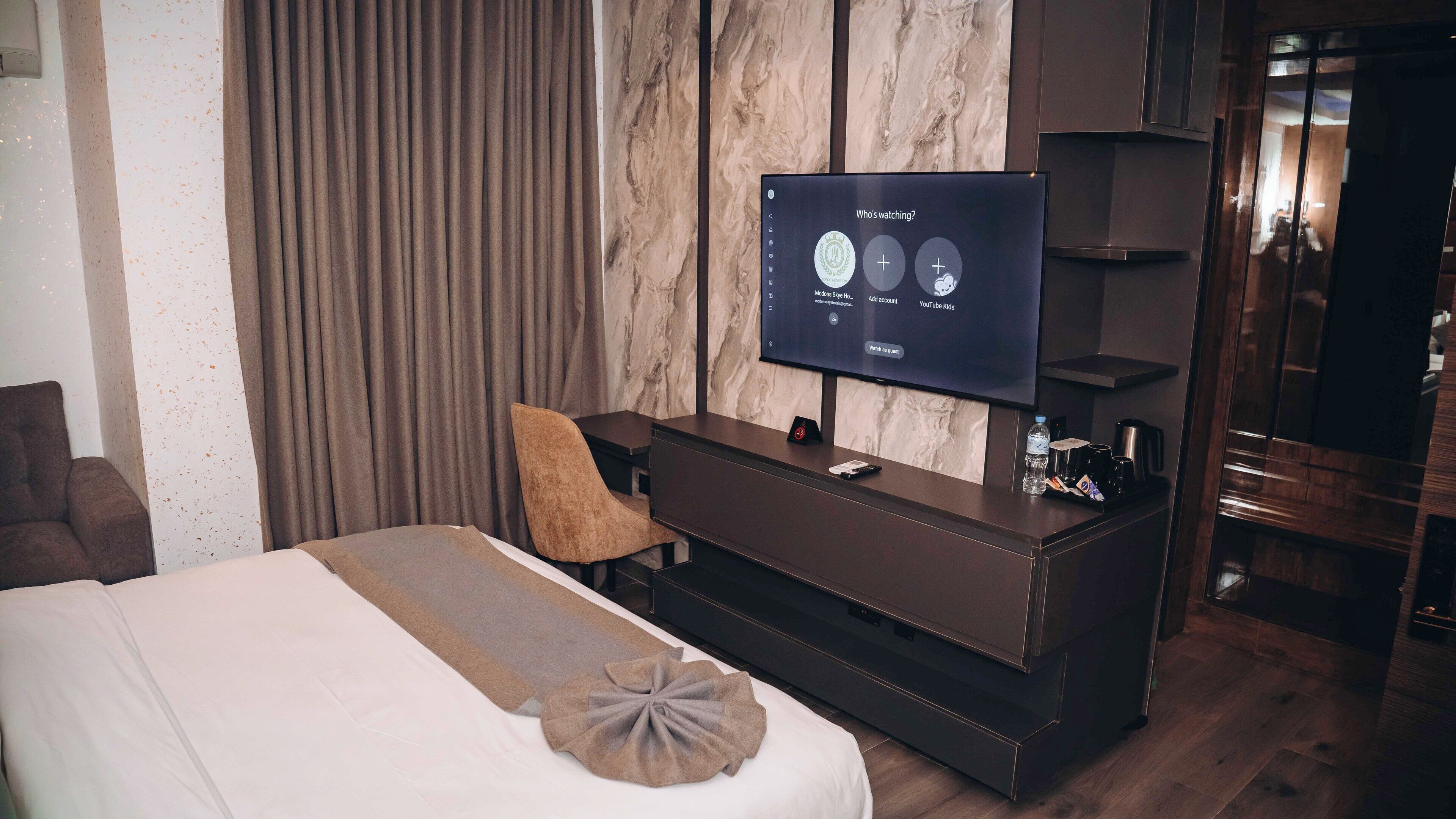 Et hotelværelse med seng, tv, siddeplads og minibar.