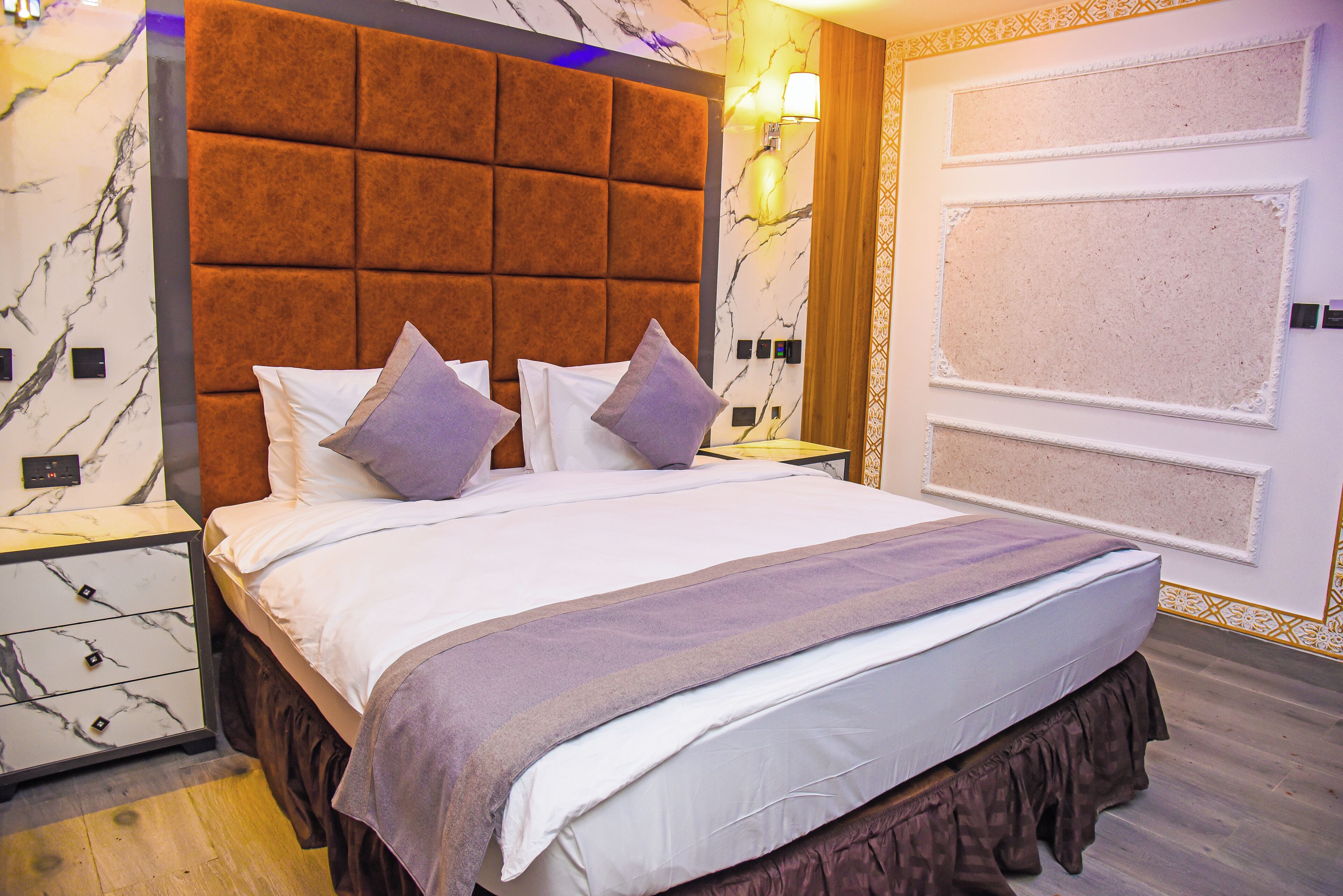 A hotel room with a large bed, a headboard, a nightstand, and a wall with a decorative panel.
