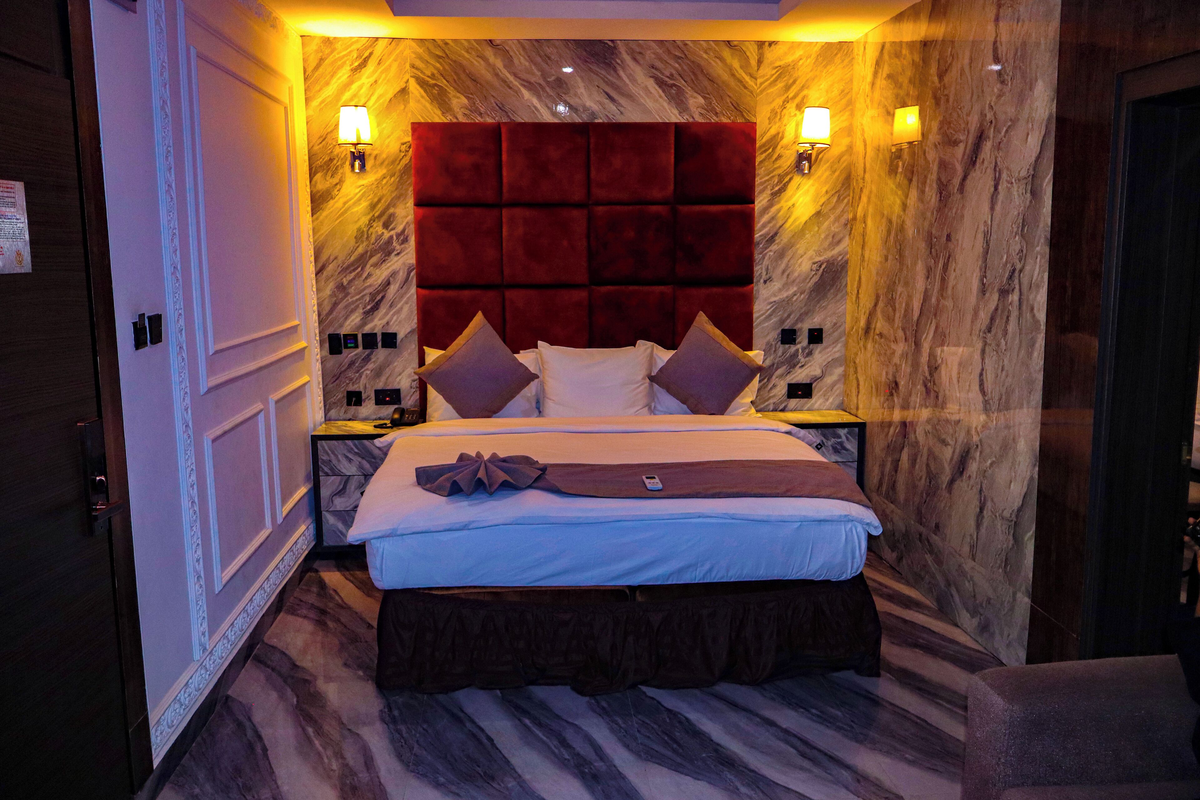 A hotel room with a marble-patterned wall, a plush red headboard, and two bedside lamps.